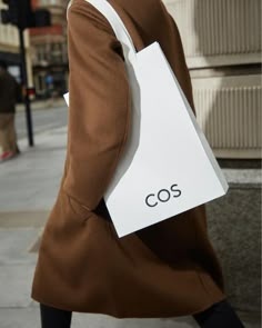 a woman walking down the street with a shopping bag in her hand and she is wearing a brown coat