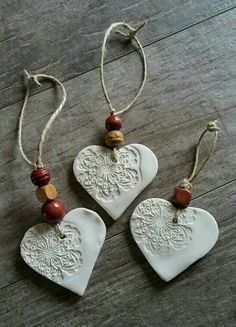 three ceramic heart ornaments hanging from strings on a wooden floor with beads and wood bead