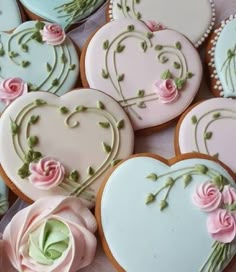 several decorated heart shaped cookies sitting on top of a table with pink roses and green leaves