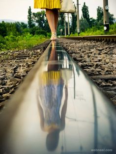 a woman walking down train tracks with her reflection in the water's puddles