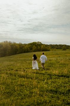 two people are running through the grass in an open field, one is flying a kite