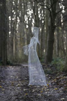 a white wire sculpture in the middle of a forest with trees and leaves on the ground