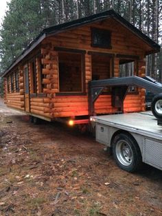 a small log cabin sits on the back of a trailer in front of some trees