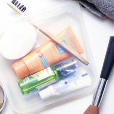 an assortment of beauty products in a plastic container next to a brush and eye shadow