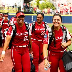 three women in red uniforms are walking on the field with their backpacks and water bottles