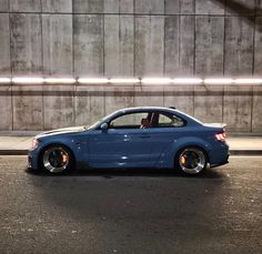 a blue car parked in front of a concrete wall at night with its door open