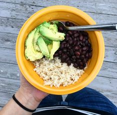 a person holding a yellow bowl filled with beans and avocado on top of rice