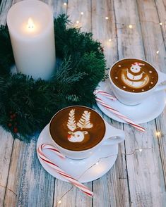 two coffee cups decorated with christmas decorations and candy canes are sitting on a table next to a lit candle