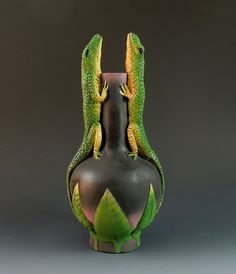 two green lizards sitting on top of a black vase with leaves around it's sides