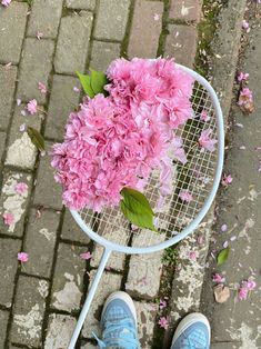 a tennis racquet with pink flowers on it and someone's feet in blue sneakers