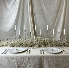 the table is set with white plates and silver utensils on it, surrounded by flowers