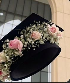 a black hat with pink roses and baby's breath on it is hanging from the ceiling