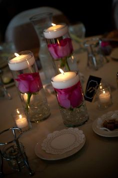 candles are lit on the table with pink flowers in vases and plates around them