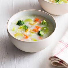 two bowls filled with soup and vegetables on top of a white table next to a napkin