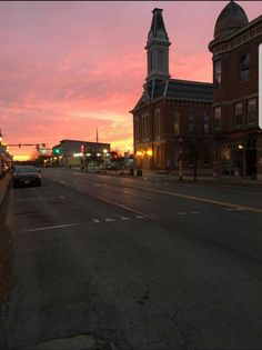 the sun is setting on an empty street with cars parked along it and buildings in the background