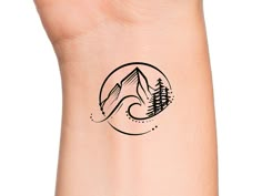 a small tattoo on the wrist of a person with mountains and trees in the background