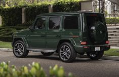 a green mercedes g - class is parked on the side of the road in front of some bushes