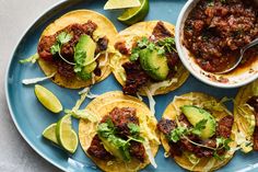 some tacos are sitting on a blue plate with a bowl of salsa and lime wedges