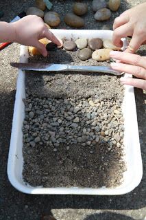 two hands reaching for rocks in a tray with a pair of scissors next to them