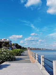 an empty walkway next to the water with buildings in the background and blue skies above