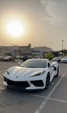 a white sports car parked in a parking lot with the sun setting behind it and buildings