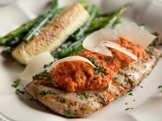 a white plate topped with fish covered in sauce next to asparagus