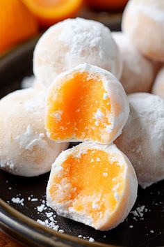 powdered sugar coated pastries on a black plate with oranges in the background