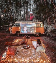 two people sitting on a blanket in front of a vw bus with a screen