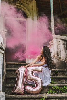 a woman sitting on the steps holding a large number twenty five balloon in front of her