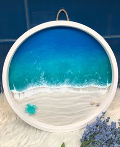 a beach scene with blue water and white sand in a circular frame, surrounded by lavender flowers