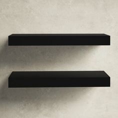 two black shelves on the wall with one empty shelf