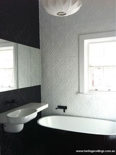 a white bath tub sitting next to a sink under a window in a bathroom with black and white walls