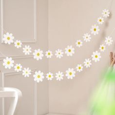 a woman is hanging daisies on a string in a room with a chair and table