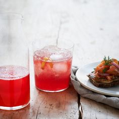 two glasses and a plate with food on it next to a pitcher filled with liquid