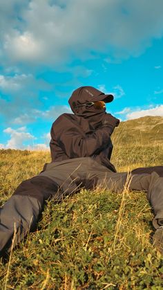 a person laying in the grass with a hat on their head and wearing a black jacket