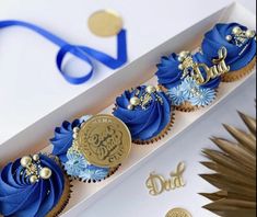 a blue and gold decorated cupcake in a white box with the word dad written on it