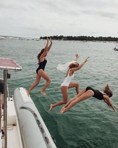 three girls jumping into the air from a boat in the water while another girl watches