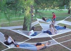 several people laying in hammocks on the ground with trees and grass behind them