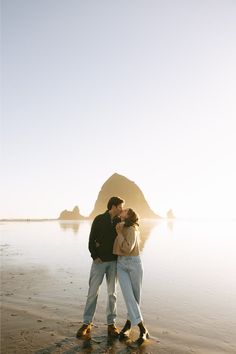 a man and woman kissing on the beach with an island in the background at sunset