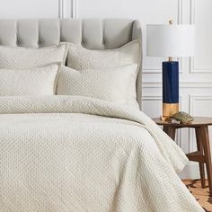 a bed with white bedspread and pillows on top of it next to a night stand