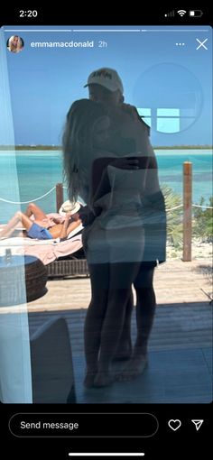 two people are standing in front of a window looking out at the beach and water