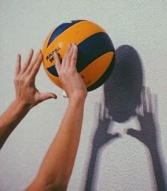 two hands reaching for a yellow and blue beach ball on the side of a wall