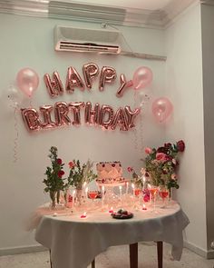 a birthday party with balloons, candles and flowers on a table in front of a sign that says happy birthday