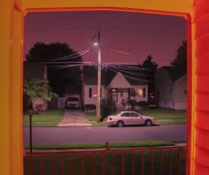 a car is parked on the street in front of a house at night with its lights on