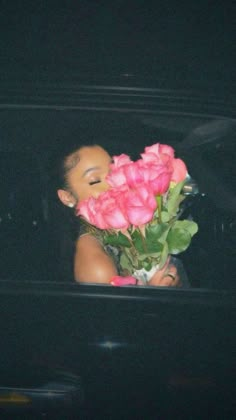 a woman is holding pink roses in the back of a truck at night, with her eyes closed