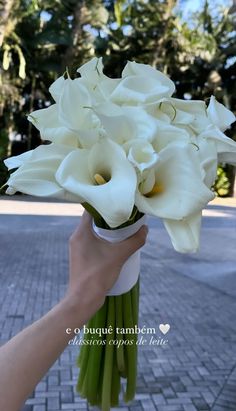 white flowers in a vase being held by a person's hand on a brick walkway