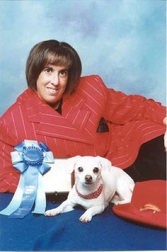 the woman is posing with her dog for a photo in front of blue backdrop and red hat