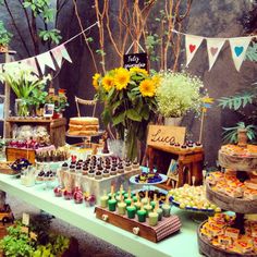 a table topped with lots of desserts next to flowers and bunting banners on the wall