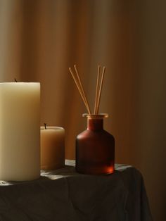 two candles sitting on top of a table next to a vase with sticks in it