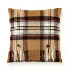 a plaid pillow with buttons and fringes on the front, sitting against a white wall